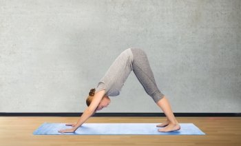 fitness, sport, people and healthy lifestyle concept - woman making yoga in downward facing dog pose on mat over gym room background