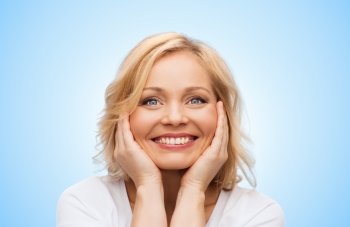 beauty, people and skincare concept - smiling middle aged woman in white shirt touching face over blue background