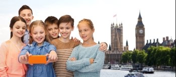 childhood, travel, tourism, technology and people concept - happy children talking selfie by smartphone over london city background