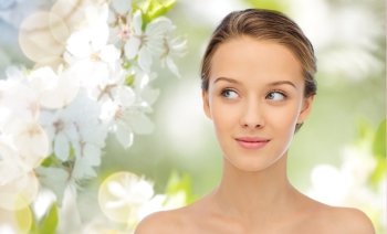 beauty, people and health concept - smiling young woman face and shoulders over summer green natural background with cherry blossom