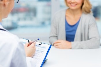 medicine, health care and people concept - close up of doctor with clipboard and young woman patient meeting at hospital