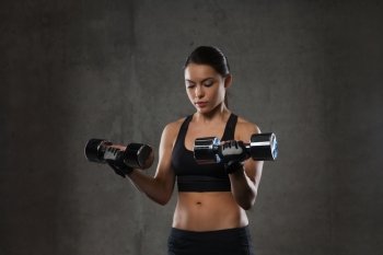 fitness, sport, exercising, training and people concept - young woman flexing muscles with dumbbells in gym