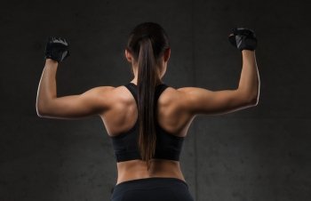 sport, fitness, bodybuilding, weightlifting and people concept - young woman flexing muscles in gym