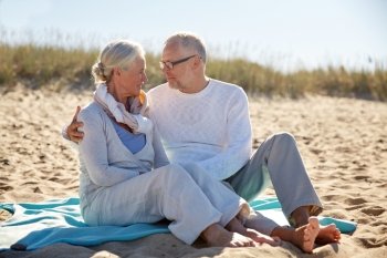 family, age, travel, tourism and people concept - happy senior couple sitting on plaid and hugging on summer beach