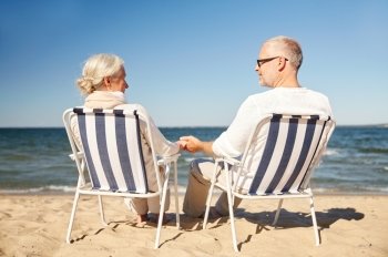 family, age, travel, tourism and people concept - happy senior couple resting in folding chairs on summer beach from back