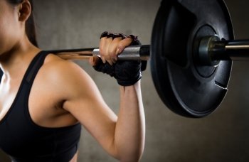 sport, fitness, bodybuilding, weightlifting and people concept - close up of young woman with barbell flexing muscles in gym