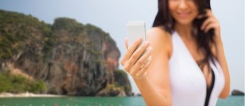 summer, travel, technology and people concept - close up of sexy young woman taking selfie with smartphone over bali beach and rock background