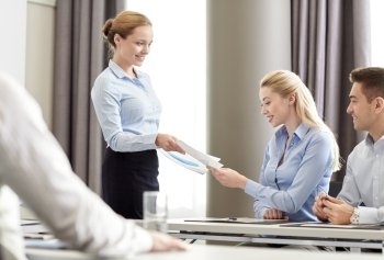 business, people and teamwork concept - smiling woman giving papers to group of businessmen in office