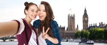 people, travel, tourism and friendship concept - happy smiling pretty teenage girls taking selfie and showing peace sign over london background