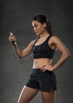 sport, fitness, technology and people concept - young woman with smartphone and earphones listening to music in gym