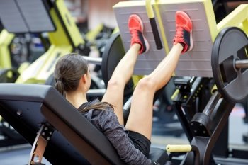 fitness, sport, bodybuilding, exercising and people concept - young woman flexing muscles on leg press machine in gym