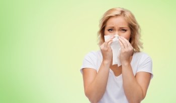 people, healthcare, rhinitis, cold and allergy concept - unhappy woman with paper napkin blowing nose over green natural background