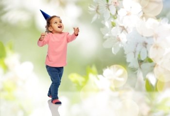 childhood, fashion, birthday, holidays and people concept - happy smiling african american little baby girl with birthday party hat playing and catching something over cherry blossoms background