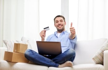 technology, people and online shopping concept - smiling man with laptop computer, parcel boxes and credit card at home showing thumbs up