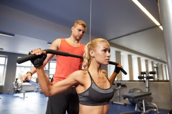sport, fitness, teamwork and people concept - young woman and personal trainer flexing muscles on cable gym machine