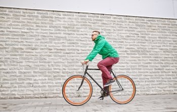 people, style, leisure and lifestyle - young hipster man riding fixed gear bike on city street over brick wall background