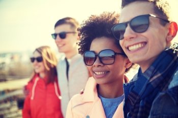 tourism, travel, people, leisure and teenage concept - group of smiling teenagers in sunglasses hugging on city street