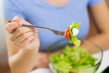 healthy eating, diet, food and people concept - close up of young woman eating vegetable salad with fork at home