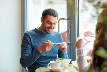 people, communication and dating concept - happy couple with smartphones picturing food at cafe or restaurant