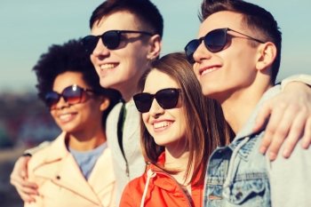 friendship, tourism, travel and people concept - group of happy teenage friends in sunglasses hugging outdoors