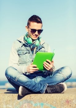 technology, lifestyle, music and people concept - smiling young man or teenage boy with tablet pc computer and headphones outdoors