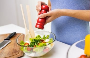 healthy eating, vegetarian food, cooking and people concept - close up of young woman seasoning vegetable salad with salt or pepper at home