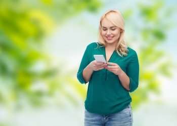 people, technology, communication and leisure concept - happy young woman with smartphone texting message over green natural background