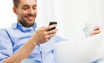 people, communication, technology and internet concept - close up of smiling man with smartphone texting or reading message and drinking tea at home