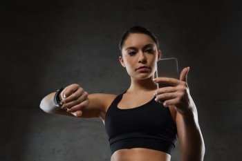 sport, fitness, technology and people concept - young woman with heart-rate watch and smartphone in gym