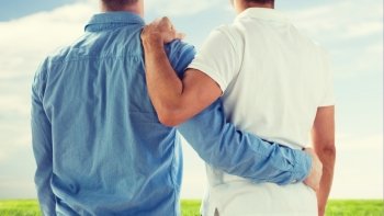 people, homosexuality, same-sex marriage, gay and love concept - close up of happy male gay couple or friends hugging from back over blue sky and grass background