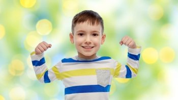 childhood, power, gesture and people concept - happy smiling little boy with raised hand over summer green lights background