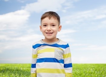 childhood, fashion, advertisement and people concept - happy smiling little boy over blue sky and green field background