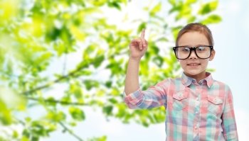childhood, environment, education, ecology and people concept - happy little girl in eyeglasses pointing finger up over green natural background