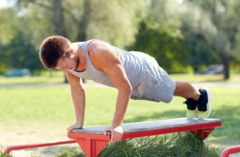 fitness, sport, exercising, training and lifestyle concept - young man doing push ups on bench at summer park