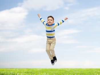 happiness, childhood, freedom, movement and people concept - happy little boy jumping in air over blue sky and grass background