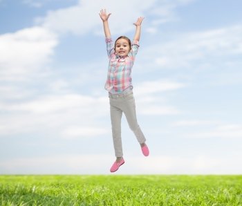 happiness, childhood, freedom, movement and people concept - happy little girl jumping in air over blue sky and grass background