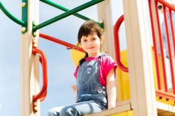 summer, childhood, leisure and people concept - happy little girl on playground climbing frame