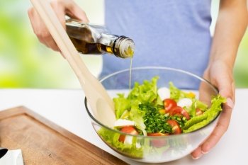 healthy eating, vegetarian food, dieting and people concept - close up of young woman dressing vegetable salad with olive oil over green natural background
