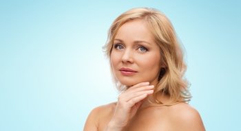 beauty, people and skincare concept - woman with bare shoulders touching face over blue background