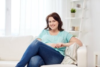 people and leisure concept - happy young woman plus size sitting on sofa at home. happy young plus size woman at home