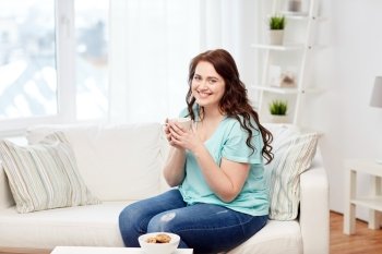people, food, eating and leisure concept - happy plus size young woman with cup of tea with cookies at home