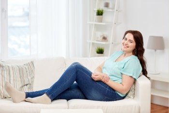 people and leisure concept - happy young woman plus size sitting on sofa at home. happy young plus size woman at home