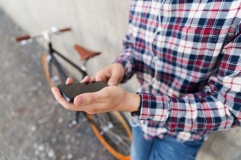 people, technology, leisure, advertisement and lifestyle - close up of young hipster man in earphones with fixed gear bike listening to music and showing smartphone black blank screen on city street