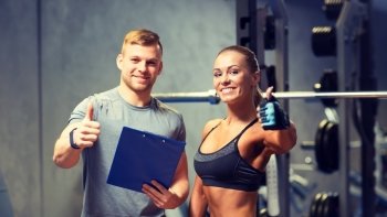 fitness, sport, exercising and diet concept - smiling young woman and personal trainer with clipboard showing thumbs up in gym