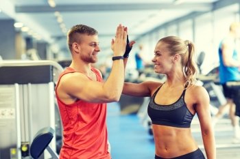 sport, fitness, lifestyle, gesture and people concept - smiling man and woman doing high five in gym