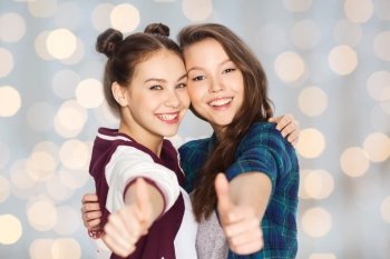 people, friends, teens and friendship concept - happy smiling pretty teenage girls hugging and showing thumbs up over holidays lights background