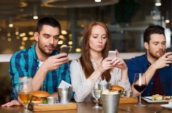 leisure, technology, lifestyle and people concept - friends with smartphones dining at restaurant
