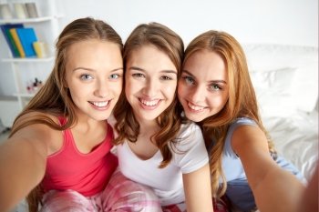 friendship, people, pajama party and fun concept - happy friends or teenage girls taking selfie at home