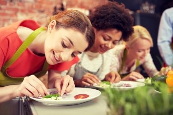 cooking class, friendship, food and people concept - happy women cooking and decorating plates with dishes in kitchen