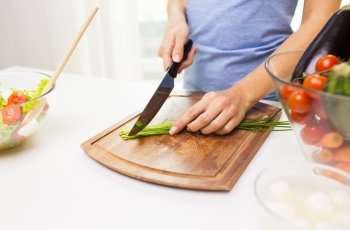 healthy eating, cooking, vegetarian food, dieting and people concept - close up of woman chopping green onion with knife on wooden cutting board